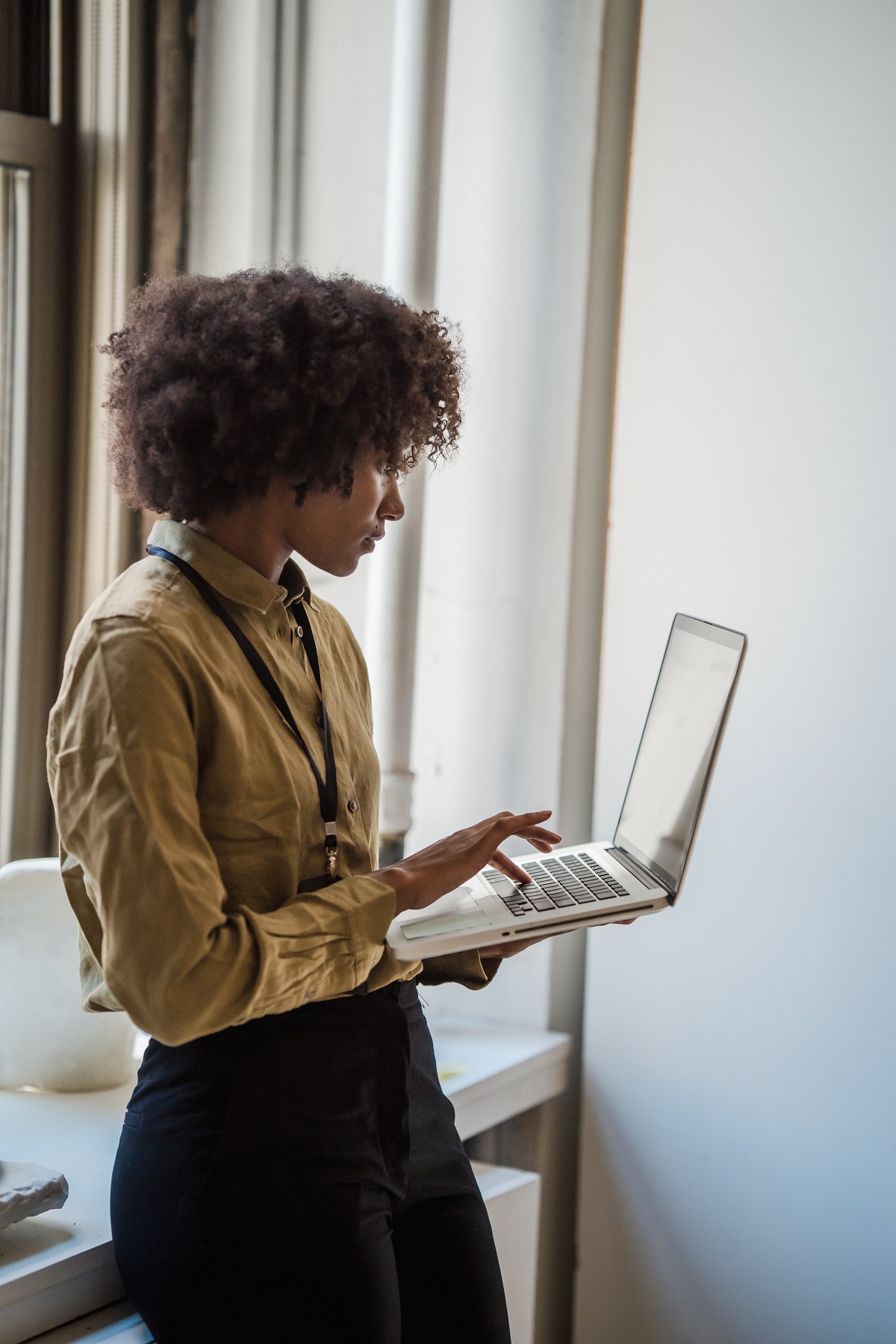 young black woman standing with laptop in hands, looking at screen contemptatively